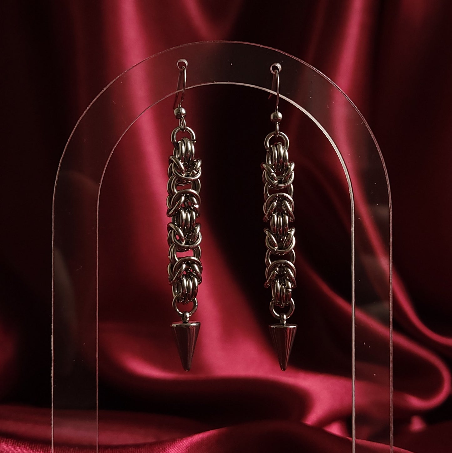 Chainmaille earrings with a spike design on a red satin background