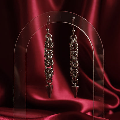 Chainmaille earrings with a spike design on a red satin background